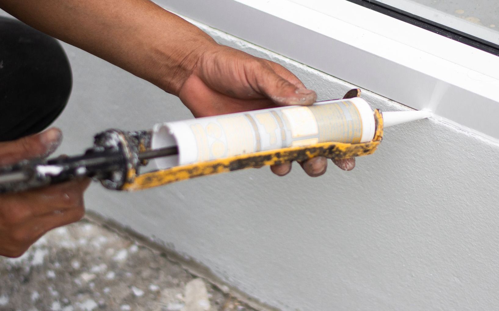 Une personne calfeutre un mur blanc avec un pistolet à calfeutrer et applique du mastic.