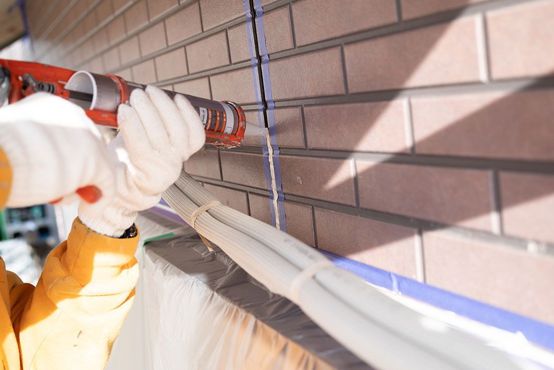 Personne appliquant du mastic sur un revêtement extérieur en briques à l'aide d'un pistolet à calfeutrer.