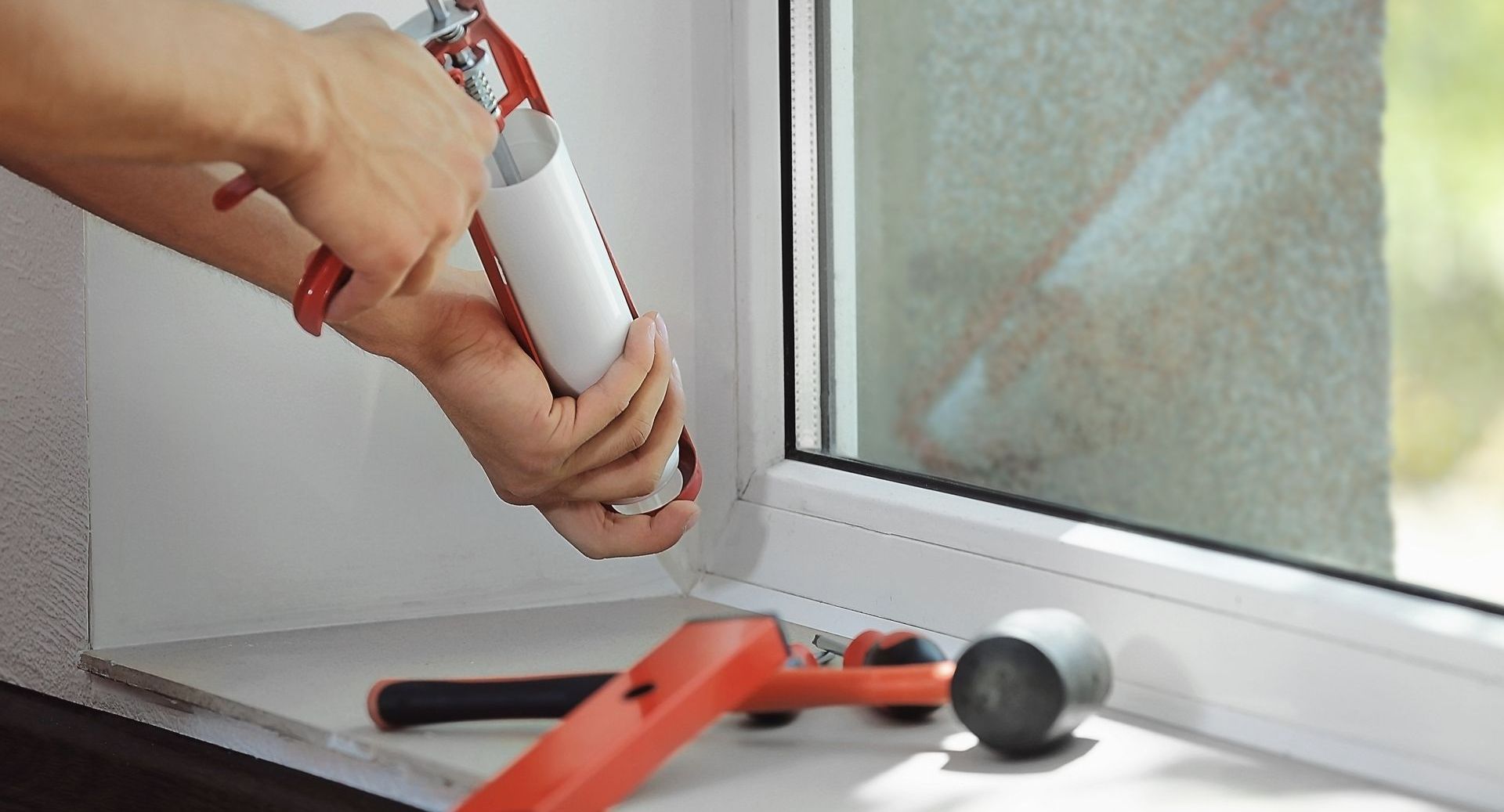Une personne applique du mastic sur le rebord d'une fenêtre.