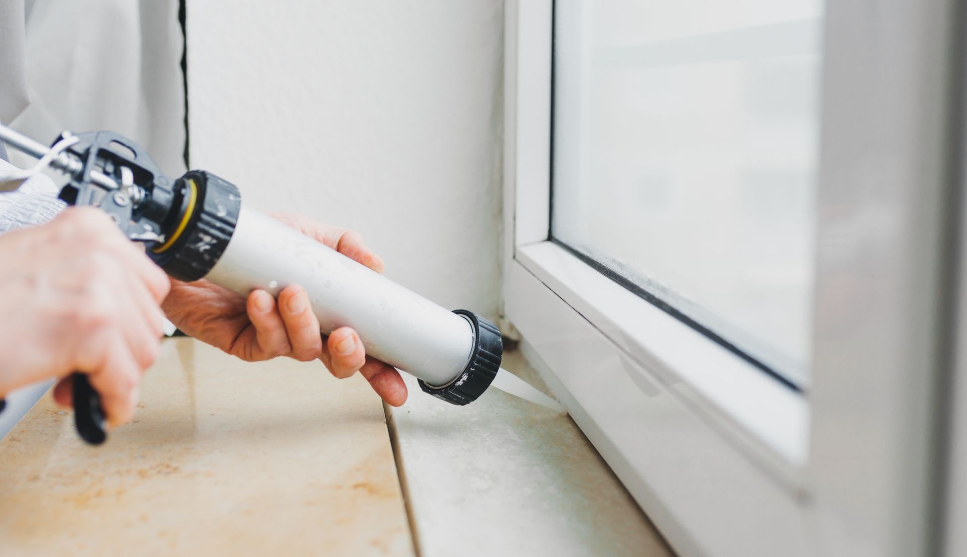 Personne scellant un cadre de fenêtre avec un pistolet à calfeutrer blanc. Intérieur, lumière naturelle.