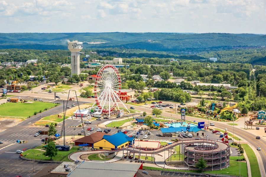 Aerial view of an amusement park with a Ferris wheel, roller coaster, and water tower surrounded by trees.
