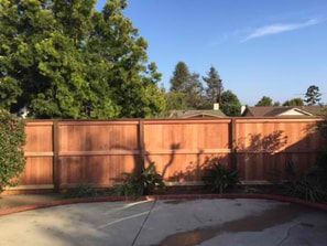 A wooden fence surrounds a patio with trees in the background.