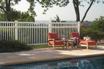 A white fence surrounds a swimming pool with chairs and a table.
