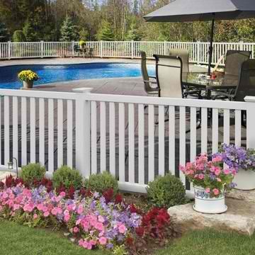 A white picket fence surrounds a lush green yard with flowers and a pool.