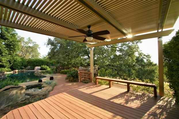 A wooden deck with a ceiling fan and a bench under a pergola.