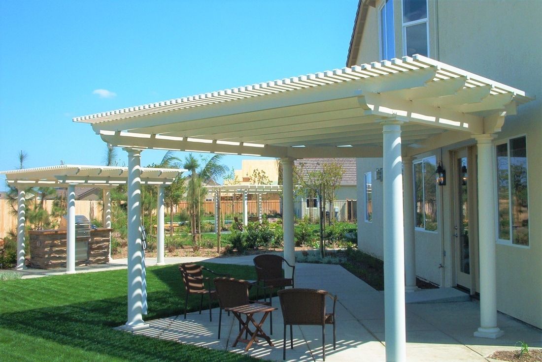 A patio with a pergola and chairs in front of a house.