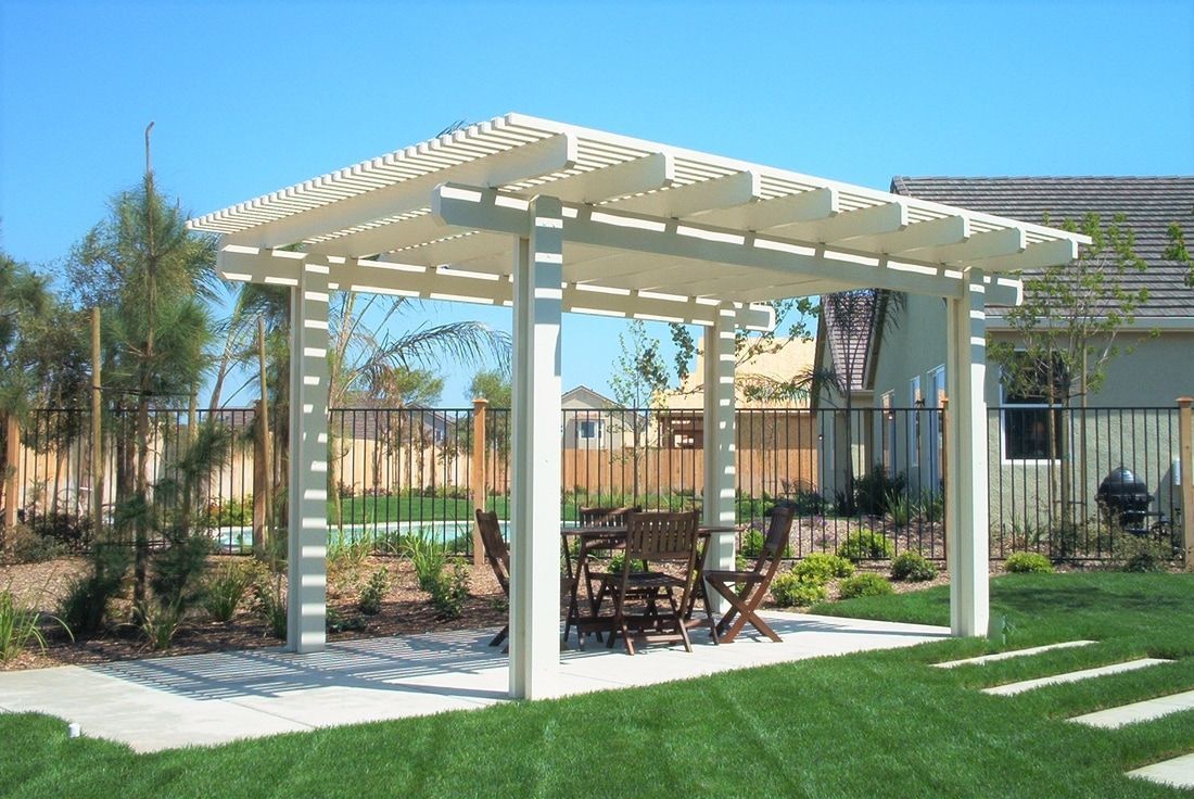 A white pergola with a table and chairs underneath it in a backyard.