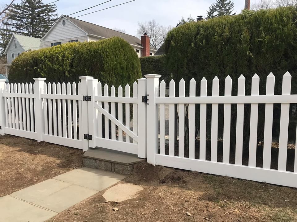 A white picket fence with a gate in front of a house.