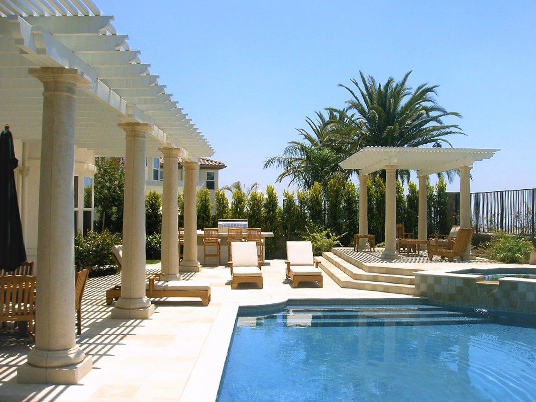 A large swimming pool is surrounded by chairs and a pergola