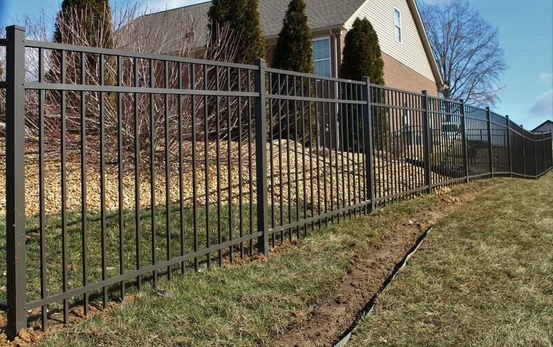 A metal fence surrounds a grassy yard in front of a house.