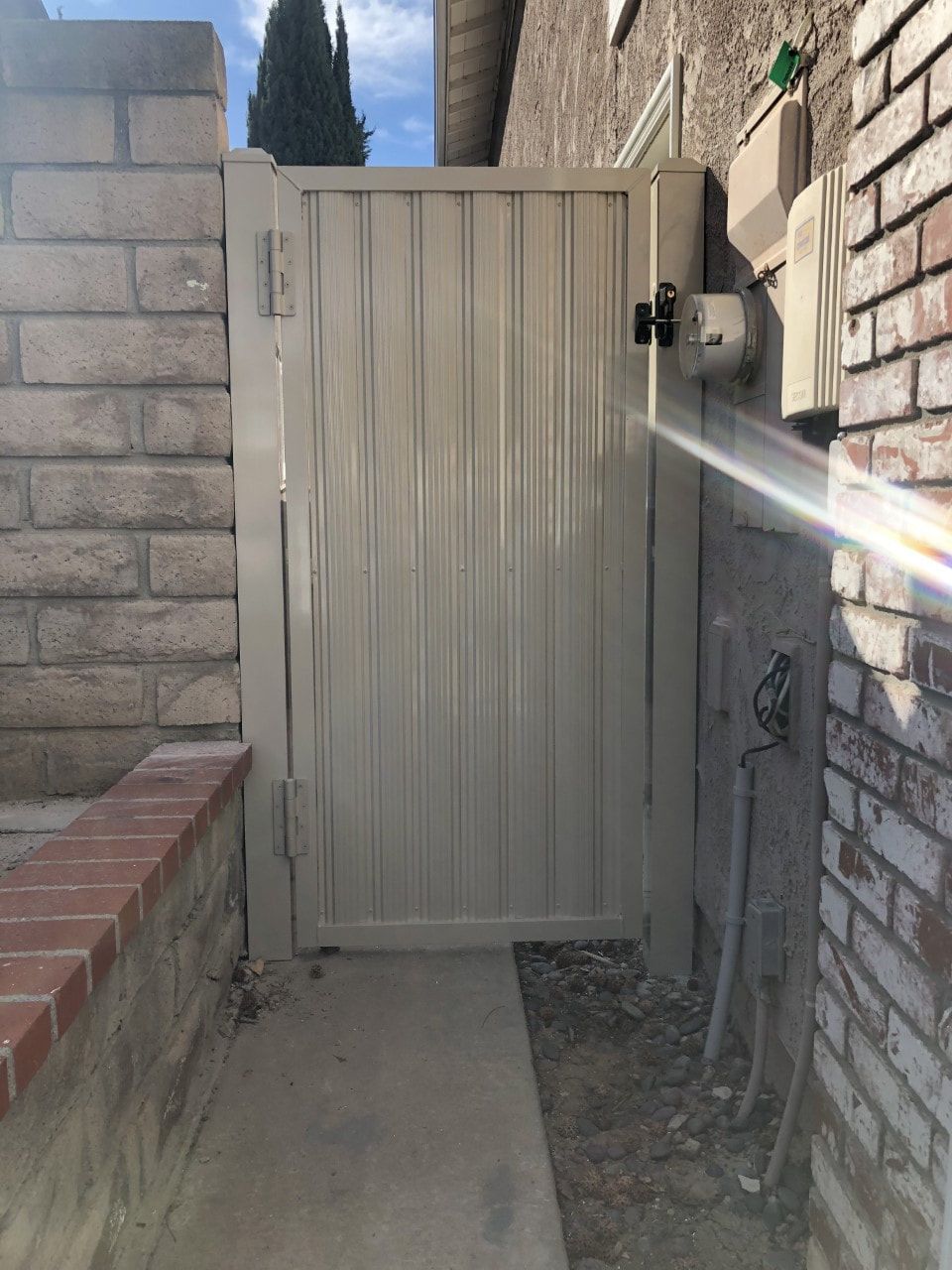 A white gate is sitting next to a brick wall.