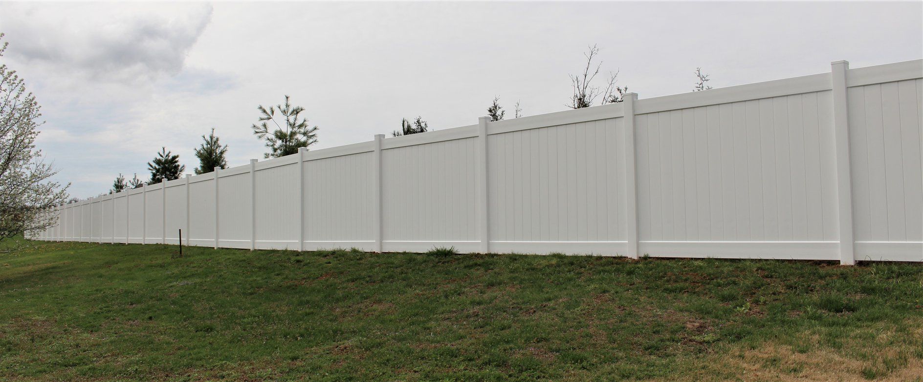 A white vinyl fence surrounds a lush green field.