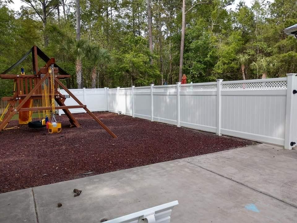 A white fence surrounds a playground with trees in the background.