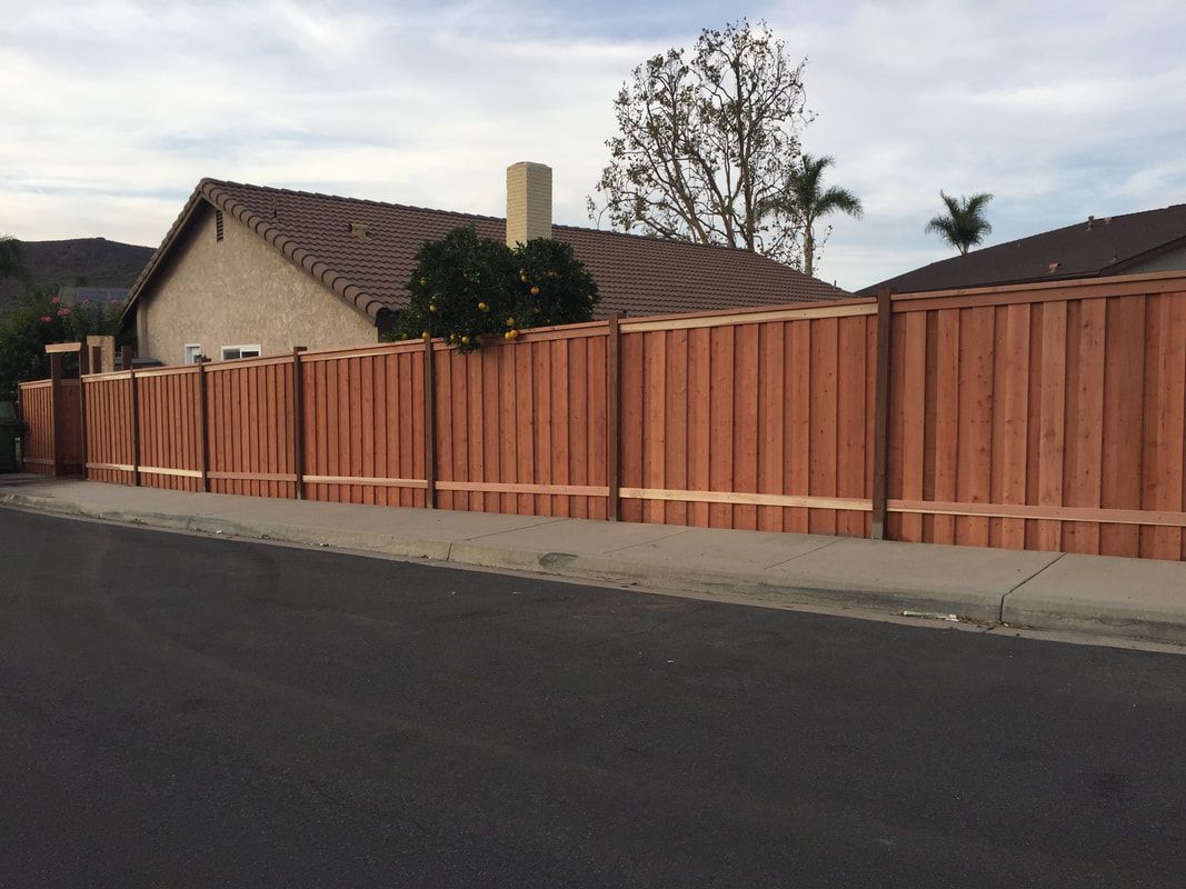 A wooden fence is along the side of a road in front of a house.
