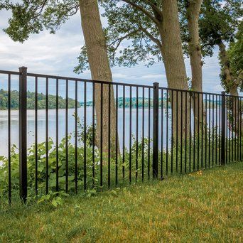 A black metal fence surrounds a lake with trees in the background.