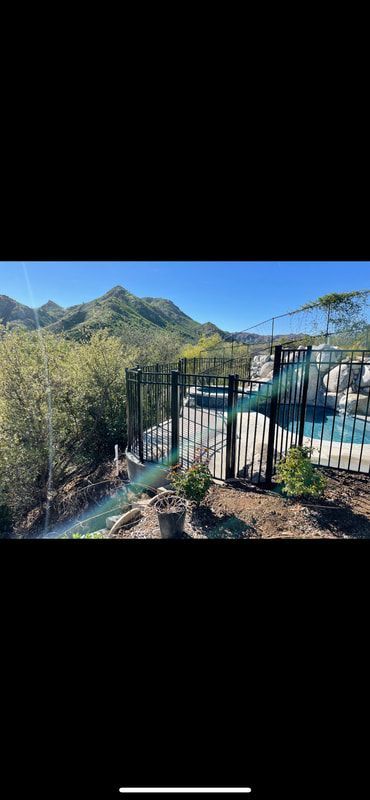 A fence surrounds a swimming pool with mountains in the background.