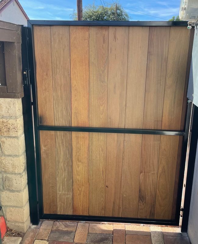 A wooden gate with a black frame is sitting next to a brick wall.