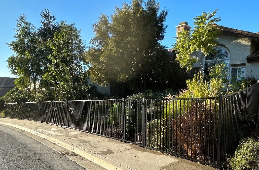 A black fence surrounds a house with trees in the background.