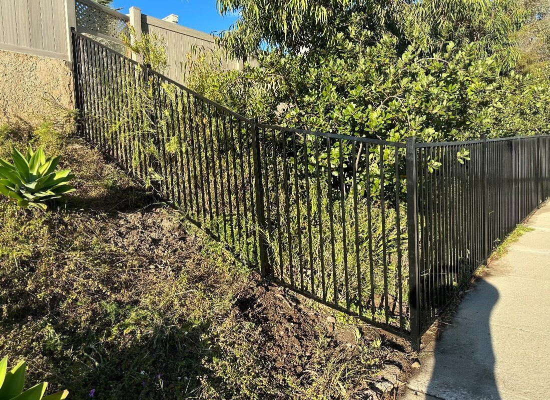 A black fence surrounds a lush green field next to a sidewalk.