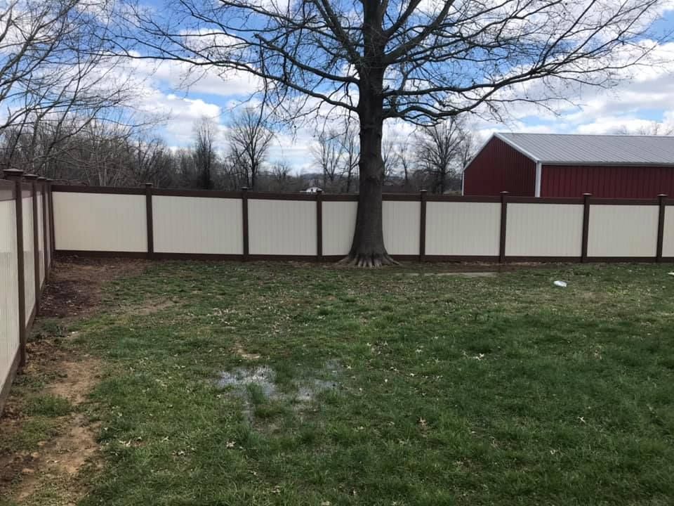 A white and brown fence surrounds a lush green yard with a red barn in the background.