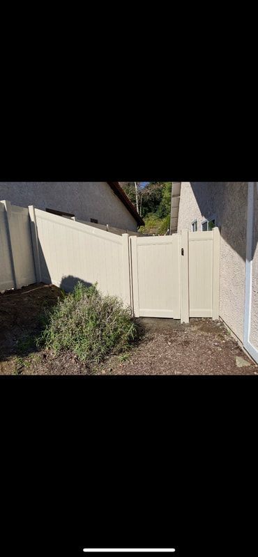 A white fence with a gate in the backyard of a house.