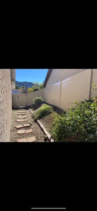 A sidewalk leading to a house with a fence and bushes.