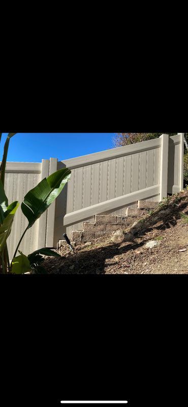 A white fence is sitting on top of a hill next to a plant.