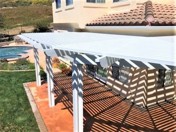 A white pergola is sitting on the side of a house next to a pool.
