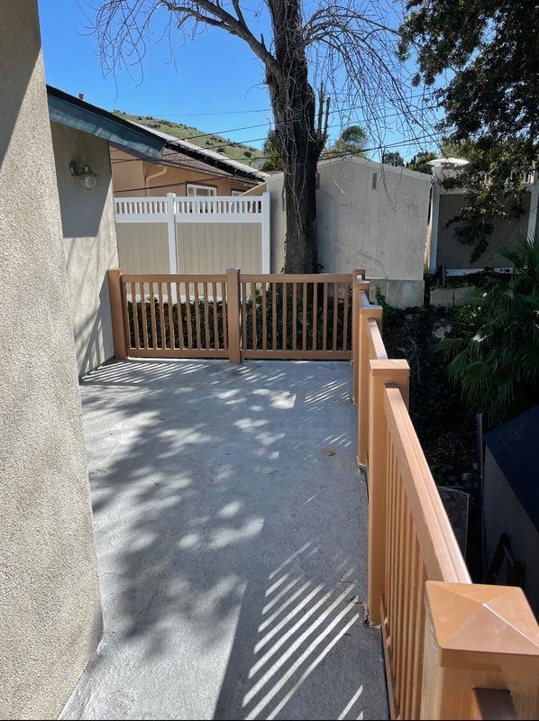 A deck with a wooden railing and a white fence
