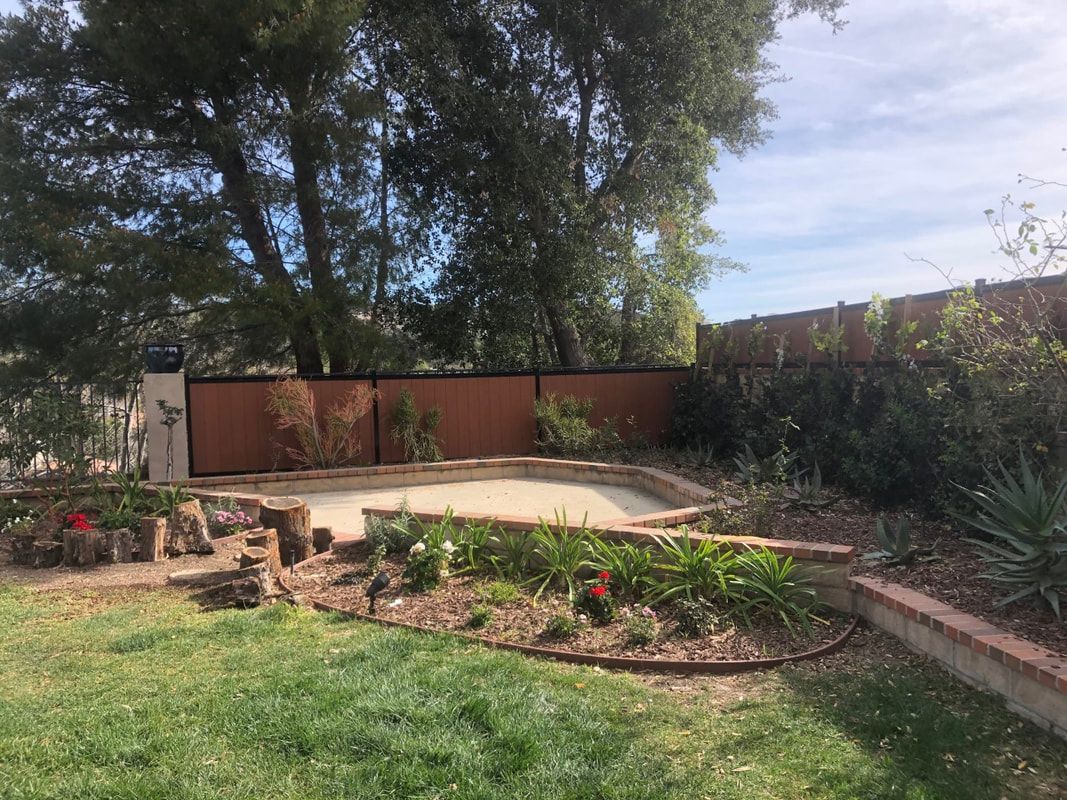A backyard with a wooden fence surrounded by trees and flowers.