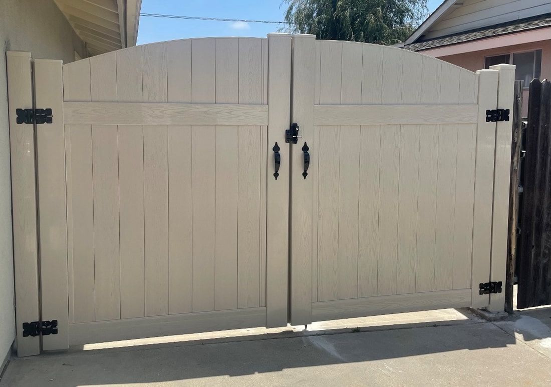 A white wooden gate with black handles is sitting in front of a house.