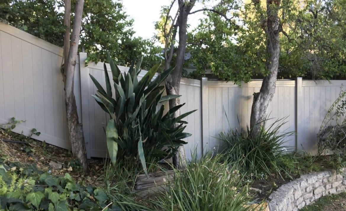 A white fence is surrounded by trees and plants in a garden.