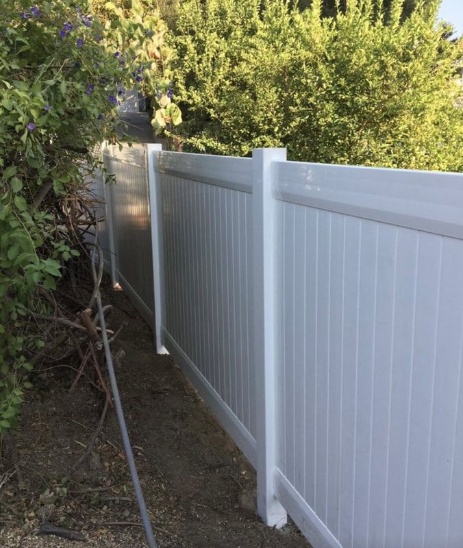 A white fence is surrounded by trees and bushes.