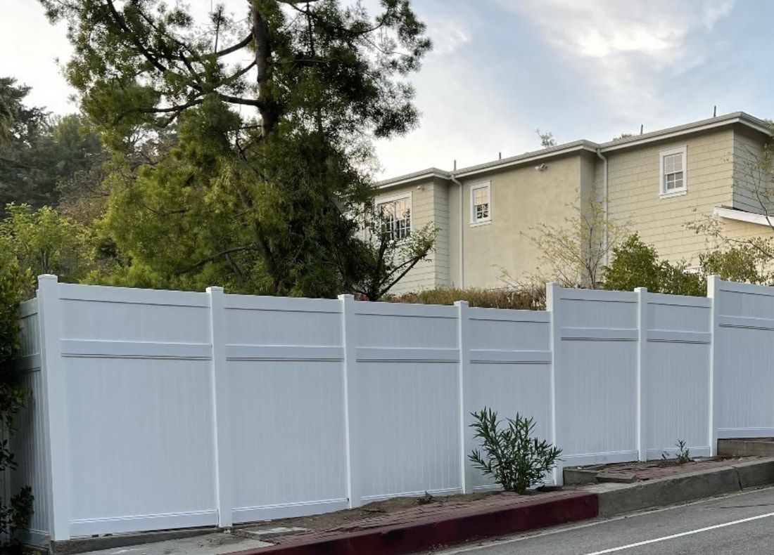 A white fence is sitting on the side of the road in front of a house.