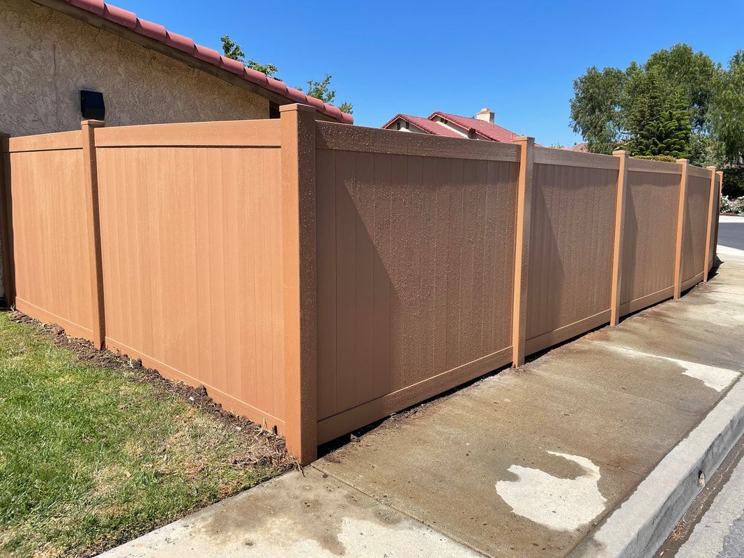 A wooden fence is sitting next to a sidewalk in front of a house.