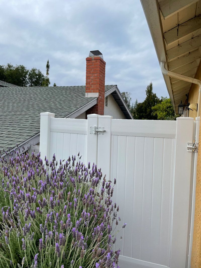 A white fence with purple flowers in front of a house.