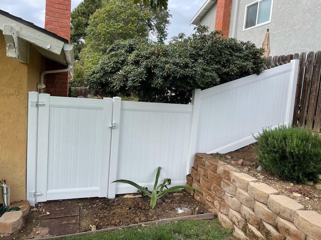 A white fence with a gate in the backyard of a house.