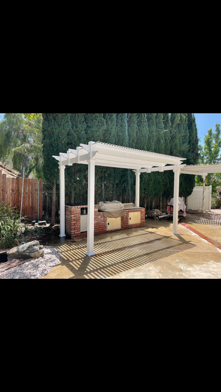 A white pergola with a grill underneath it in a backyard.