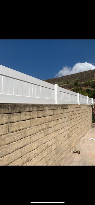 A white fence is sitting on top of a brick wall.