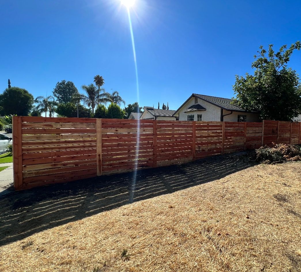 A wooden fence is sitting in the middle of a field in front of a house.