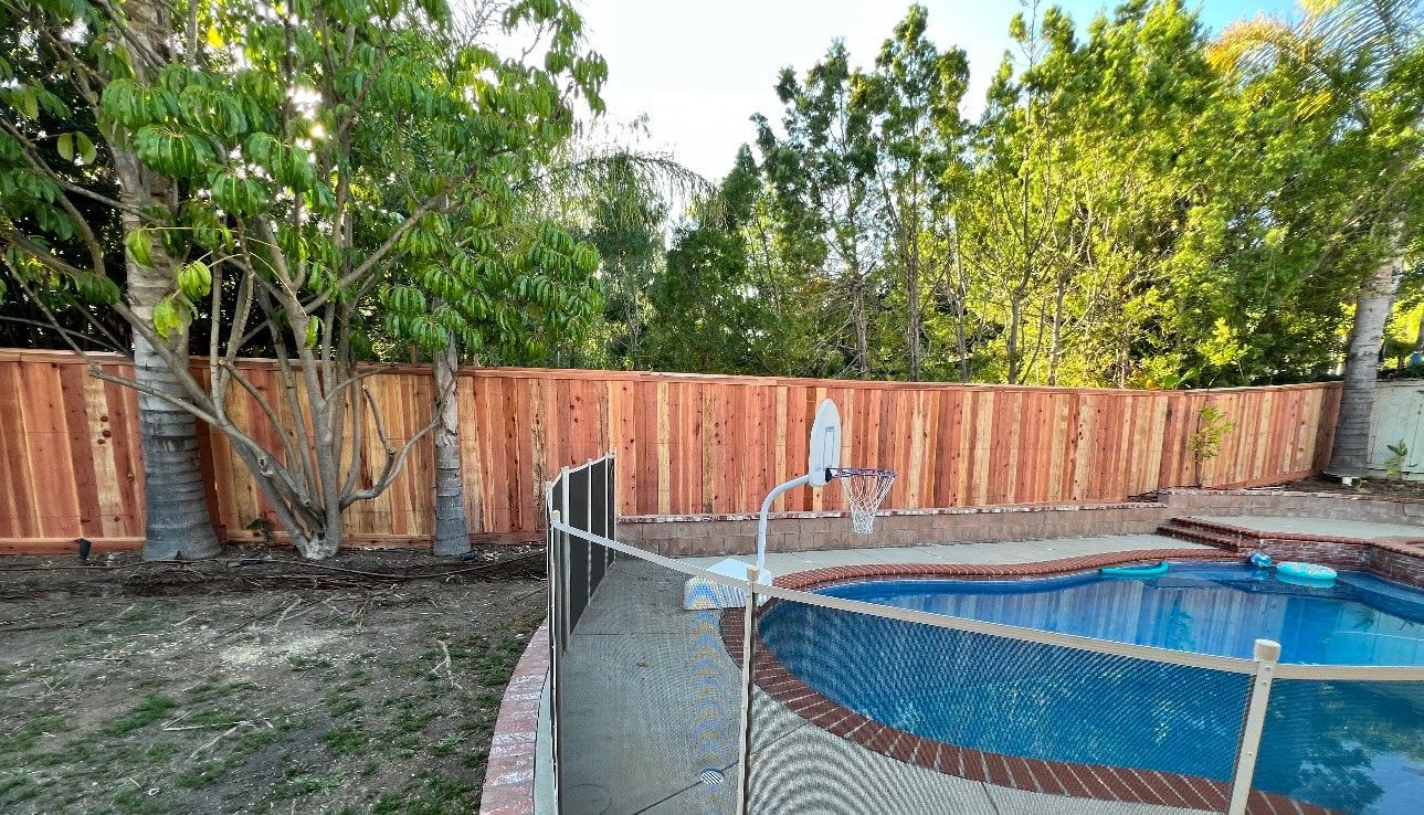 A wooden fence surrounds a swimming pool in a backyard.