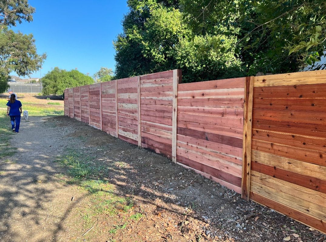 A man is walking down a dirt path next to a wooden fence.