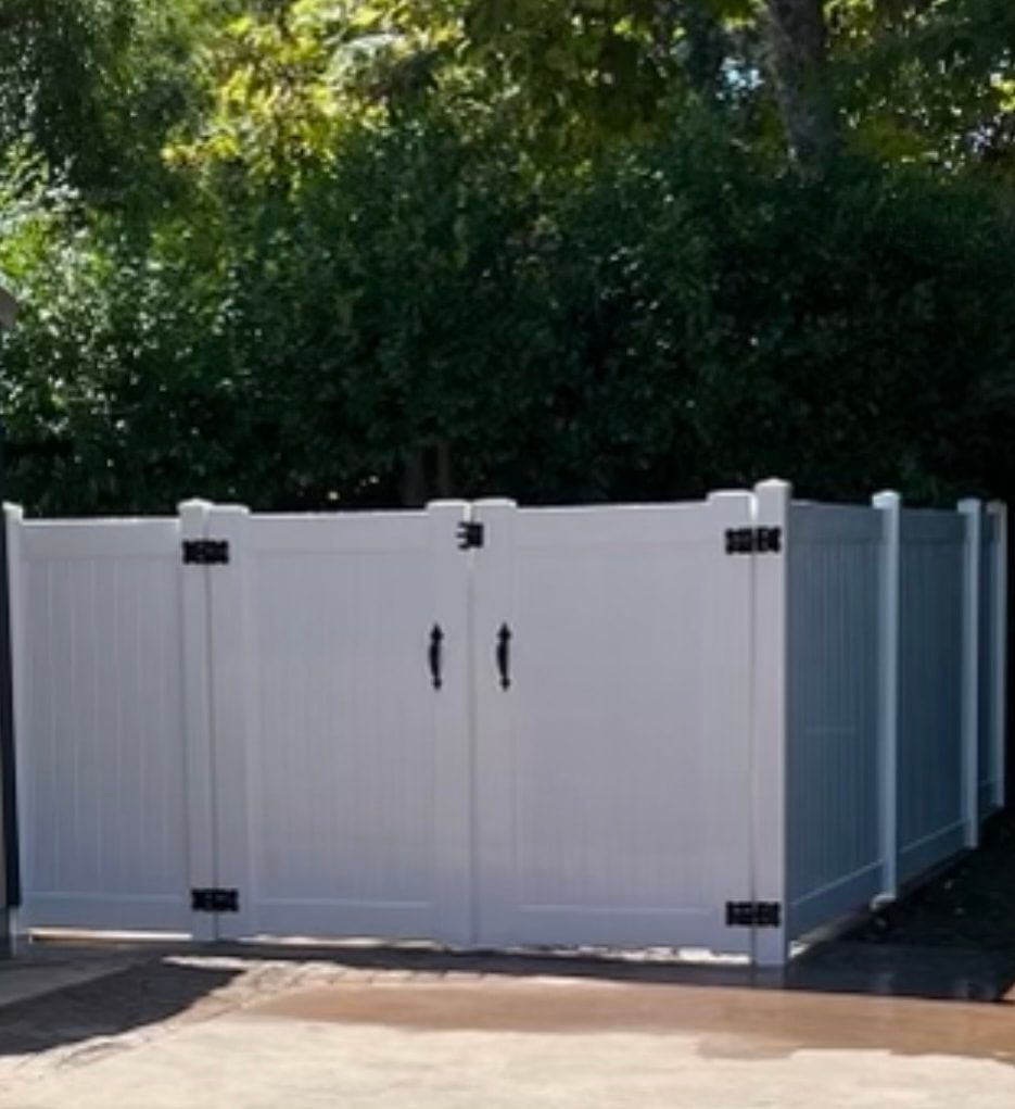 A white fence with two doors is surrounded by trees.