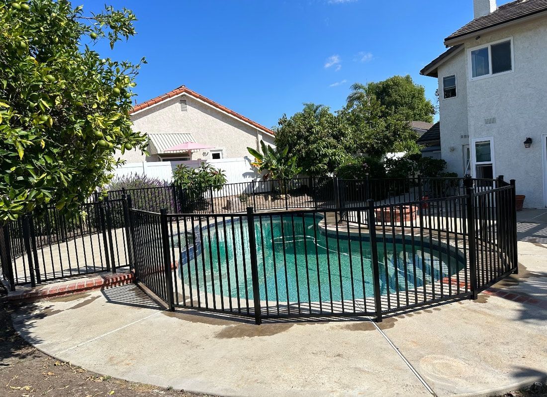 A large swimming pool surrounded by a metal fence in front of a house.