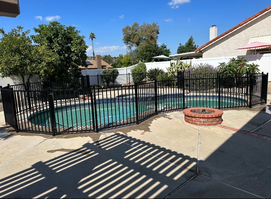 A large swimming pool surrounded by a wrought iron fence and a fire pit.