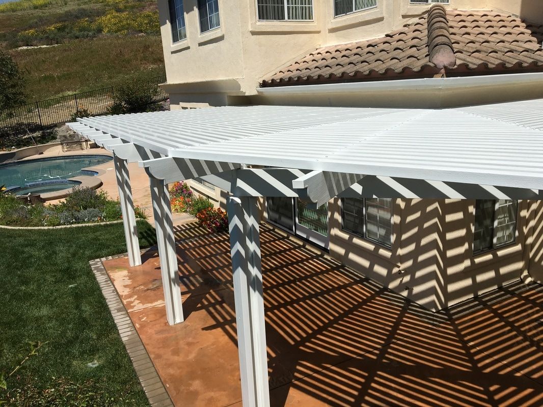 A white pergola is sitting on top of a patio next to a house.