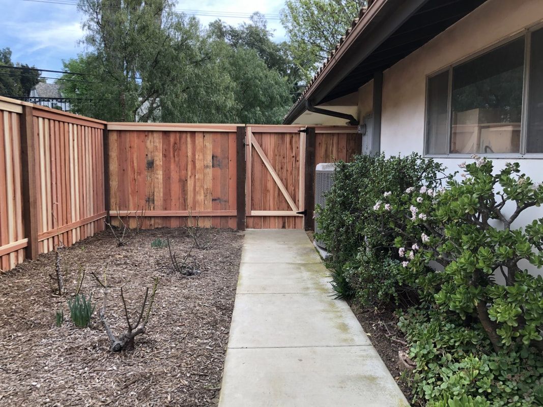 A wooden fence surrounds a concrete walkway leading to a house.