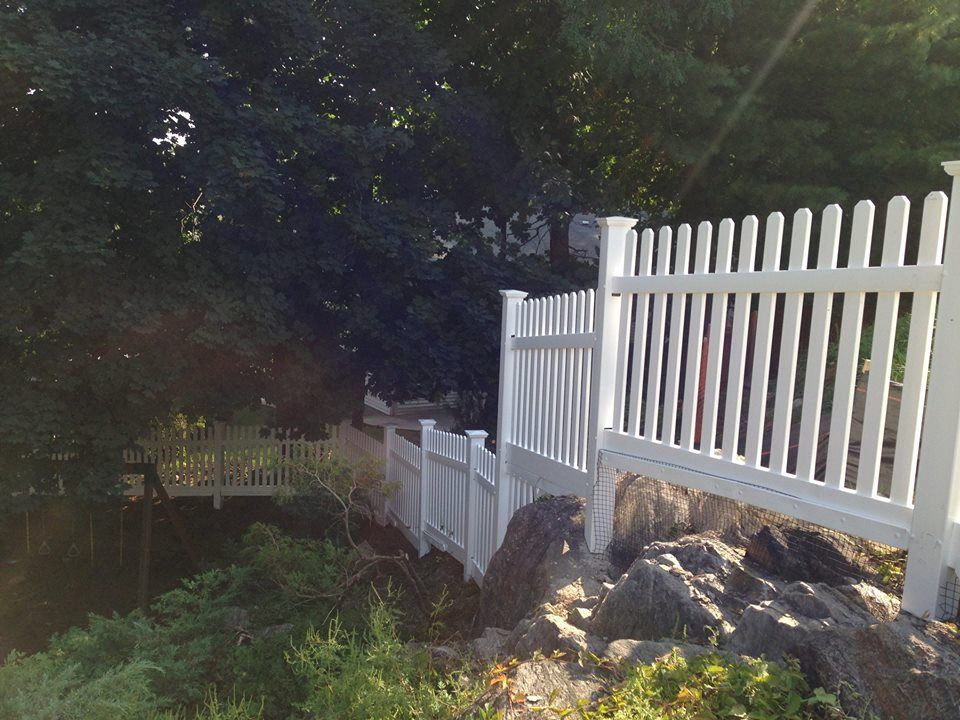 A white picket fence is surrounded by trees and rocks