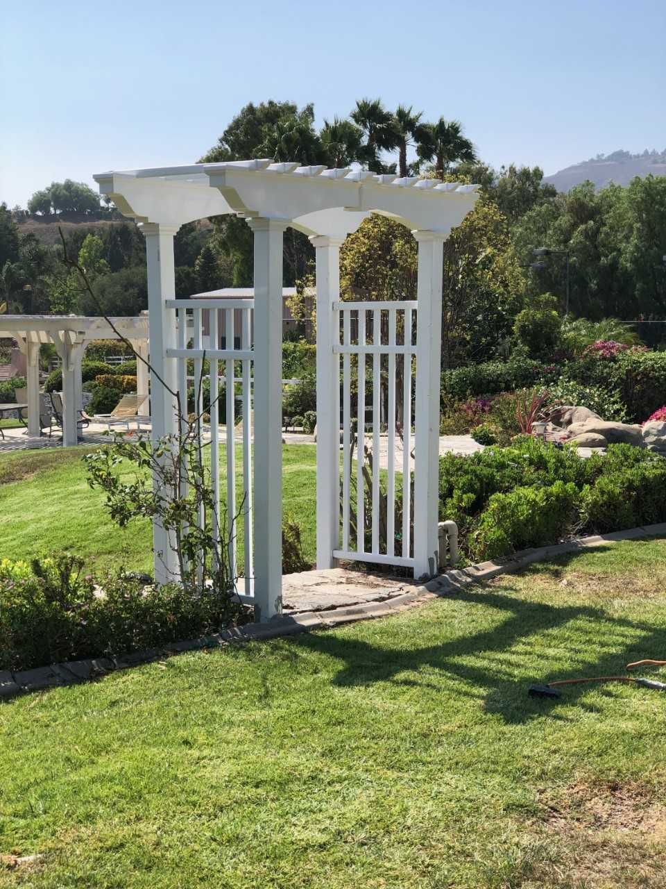 A white pergola is sitting in the middle of a lush green field.