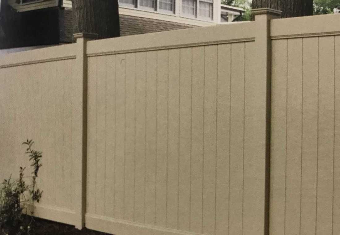 A white wooden fence is sitting next to a tree in front of a house.